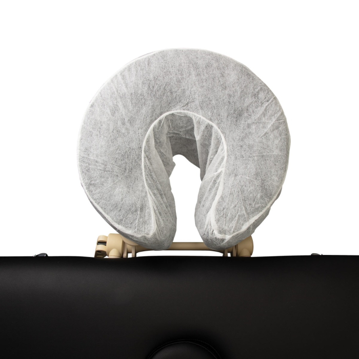 Gros plan frontal d’une table de massage noire dont le berceau facial est recouvert d’une feuille de papier blanche jetable, Housses d’Appui-Tête Jetables – Ajustées (pack de 50).